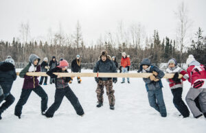A group of youth playing the Dene game called pole push in a snow-covered field.