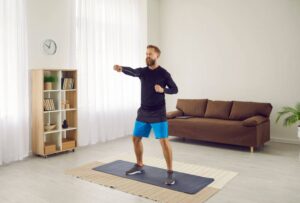 A man in exercise clothes punching the air while in a living room. 
