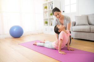A woman helping her daughter do a yoga pose on a living room floor.