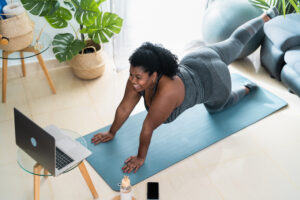 Une femme fait du yoga dans son salon et regarde l’écran d’un ordinateur portable. 