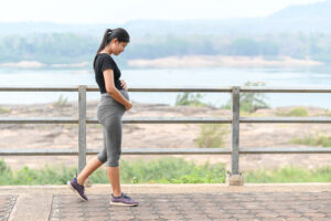 A pregnant woman walking on a path overlooking a body of water and mountains.