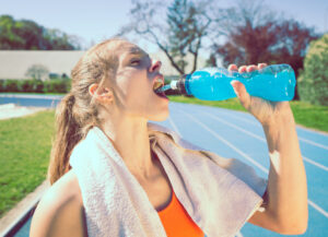 A woman drinking a sports drink while standing on an outdoor track.