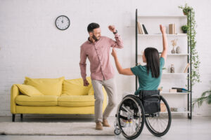 Un homme danse à côté d’une femme qui danse assise dans un fauteuil roulant. 