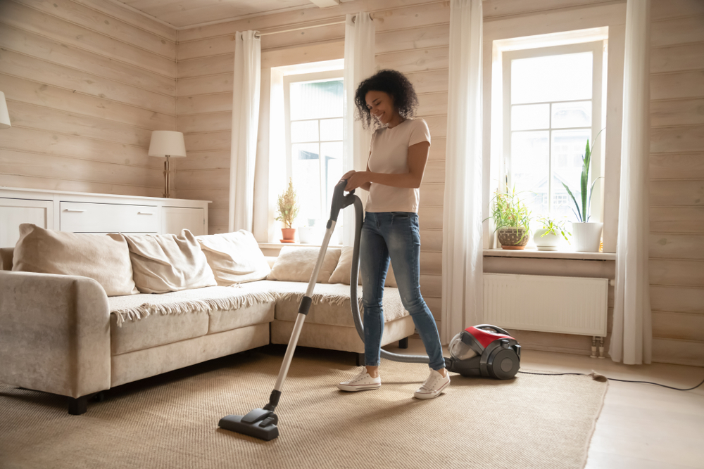 Une femme passe l’aspirateur sur un tapis dans son salon. 