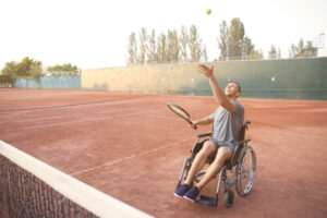 Un homme jouant au tennis en fauteuil roulant sur un terrain extérieur en terre battue.