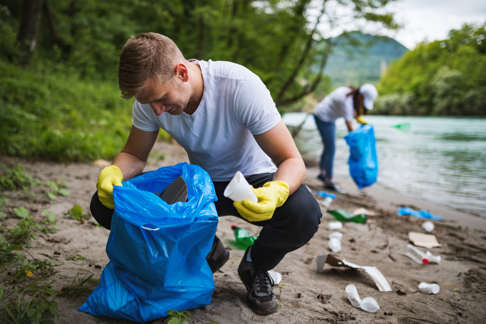 Two people picking up trash on a beach. 