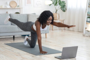 A woman doing a yoga pose in front of a laptop in a living room. Following along with online exercise videos is a great way to get active on a budget. 