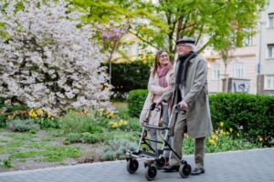 A woman walking beside an older man using a walker on a sidewalk. 