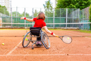Une femme jouant au tennis en fauteuil roulant sur un terrain extérieur en terre battue.