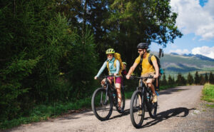 A family cycling on a gravel path surrounded by trees and mountains.