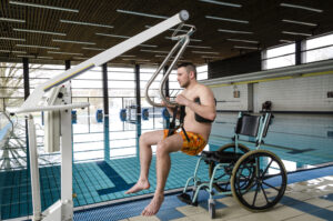 A device lifting a man from his wheelchair into an indoor swimming pool.