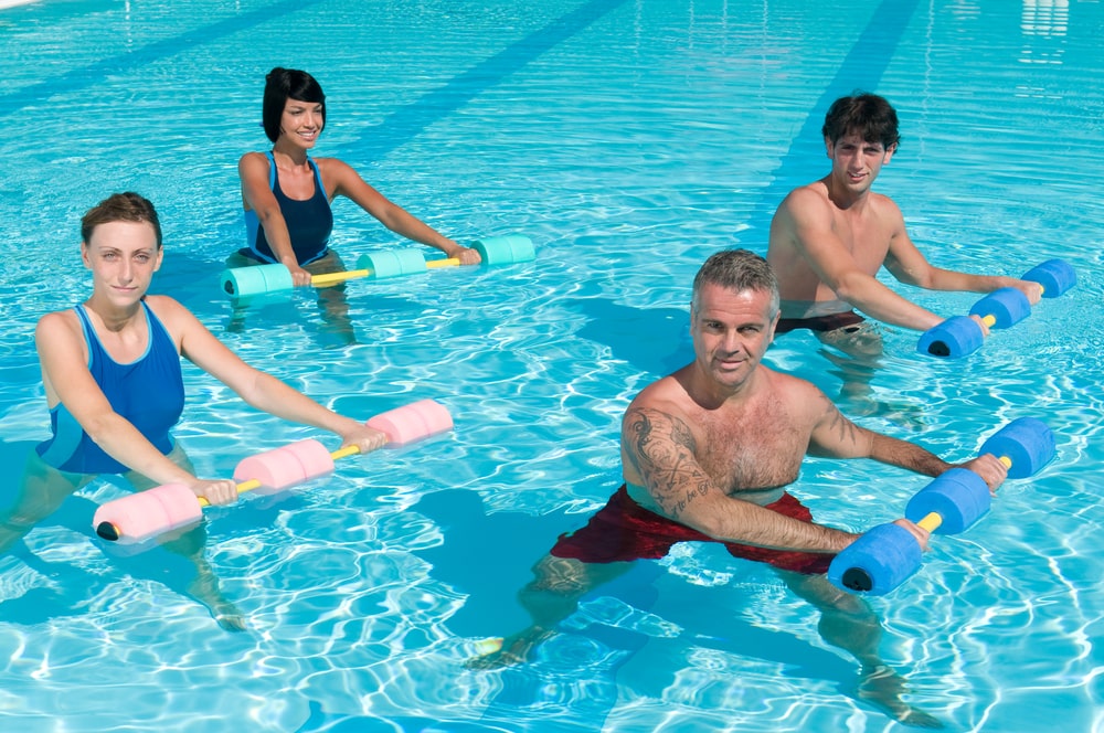 A group of people doing water aerobics, one of many water sports and activities to try this summer, in an outdoor pool. 