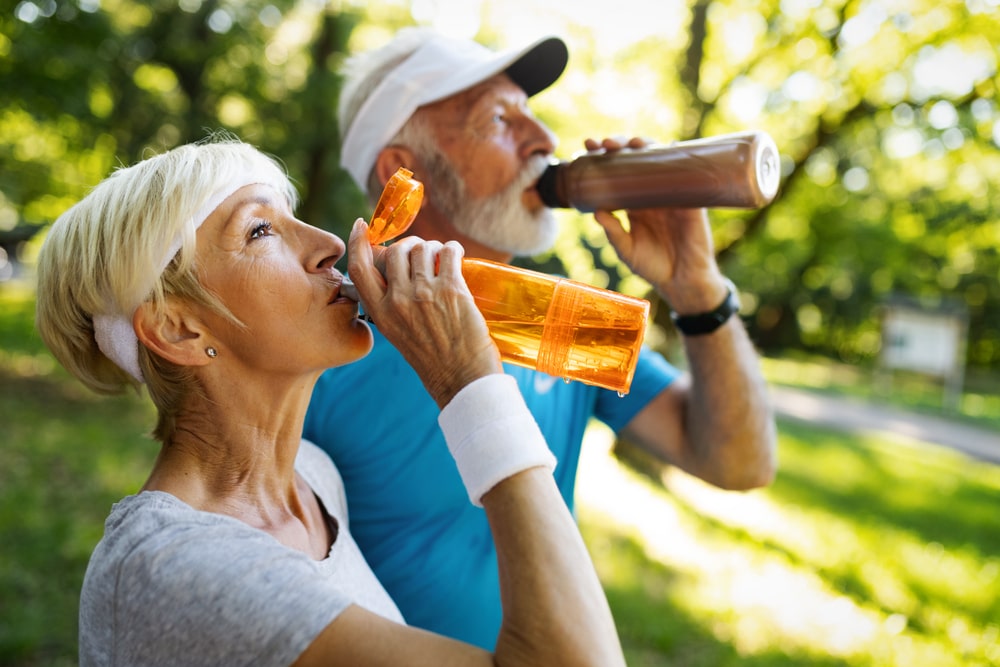 Two older adults drinking water from bottles in a park. 