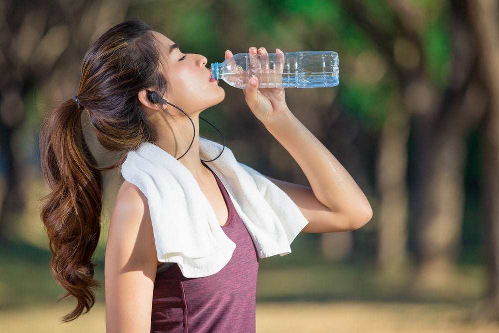 A woman in workout clothes drinking water from a bottle. 