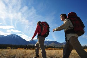 Two people hiking in a field surrounded by mountains.