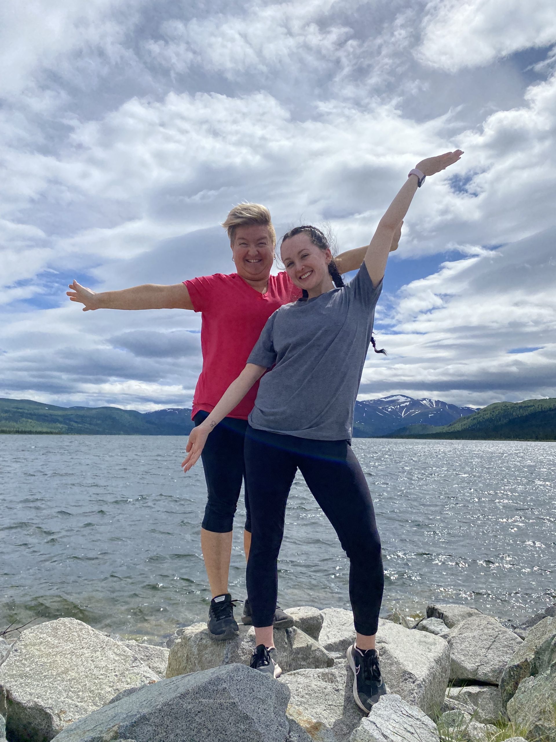 Madison and her mom standing on rocks in front of a lake surrounded by mountains. 