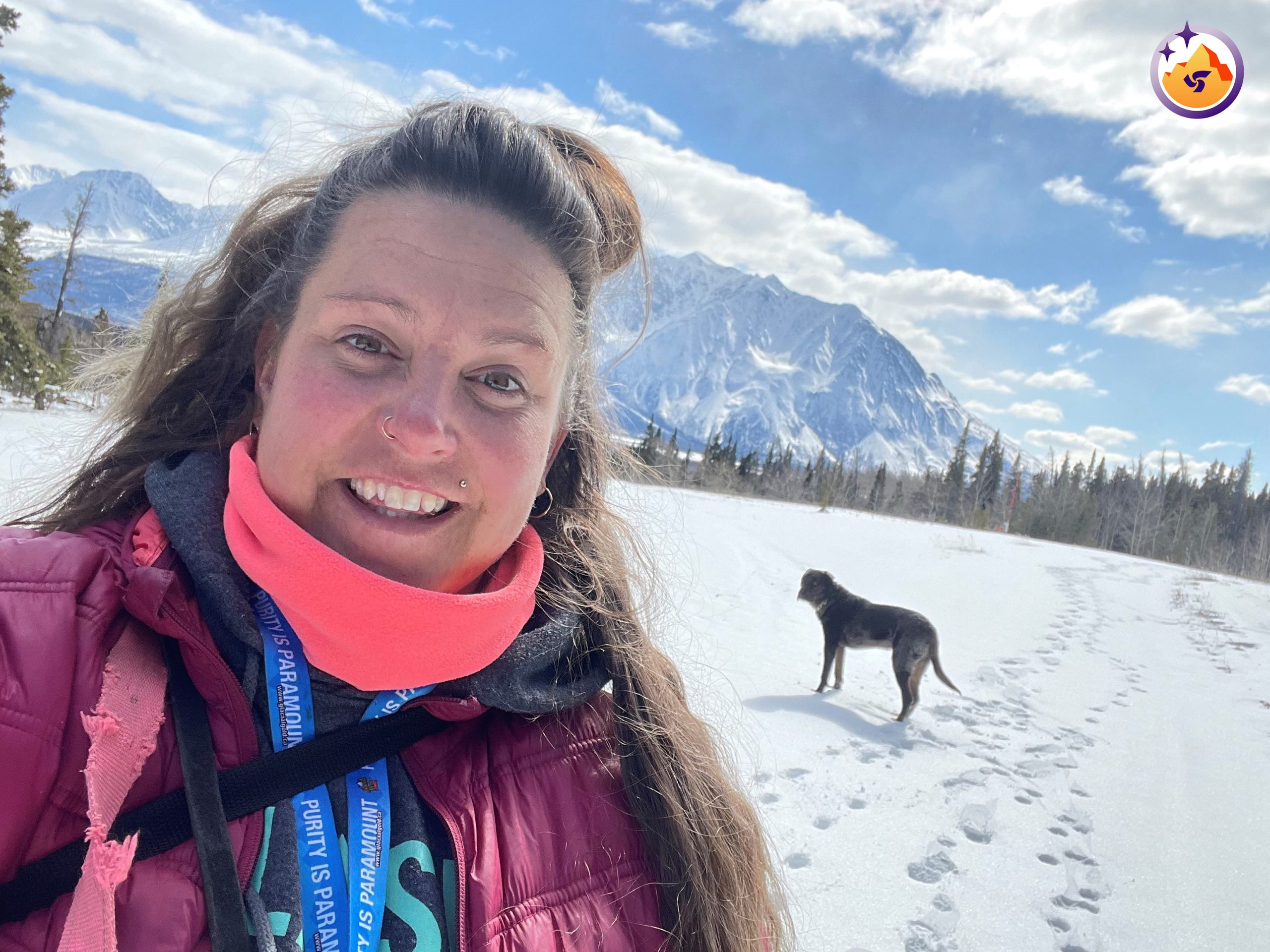Isabelle Piché debout dans un champ enneigé, avec un chien et une montagne derrière elle.