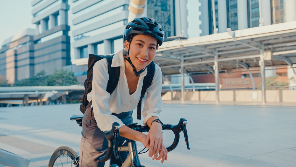 A woman in work clothes sitting on a bicycle in a city parking lot. 