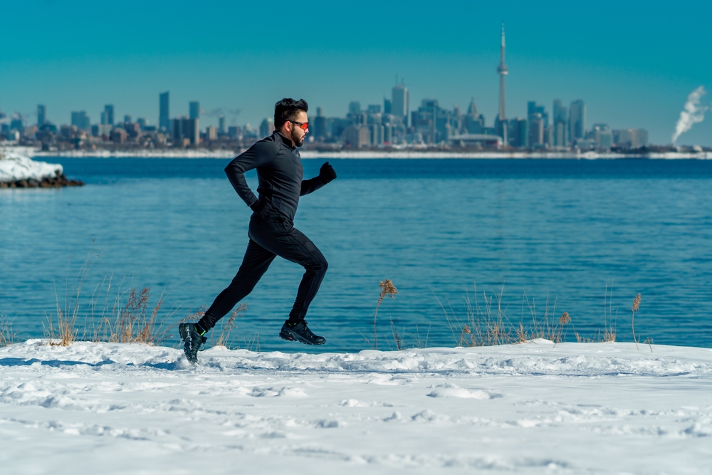 A man jogging on a snow-covered path by a lake. 