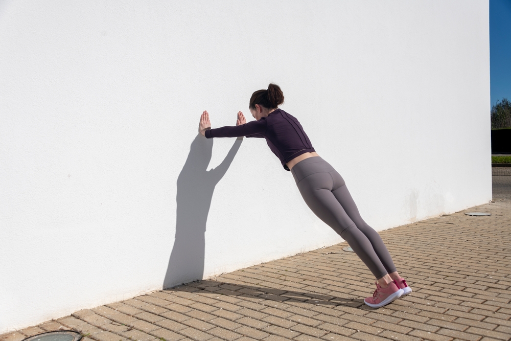 A woman doing a wall push-up outdoors. 
