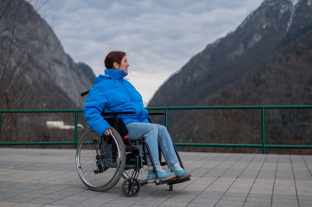 A woman in a wheelchair wheeling on a bridge with mountains in the background. 