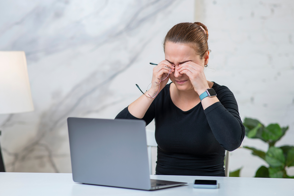 Une femme se frotte les yeux devant un ordinateur portable. Trop de temps d’écran peut entraîner une fatigue oculaire. 