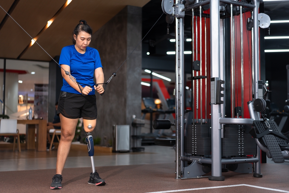 A woman with a prosthetic leg using an exercise machine at a gym.