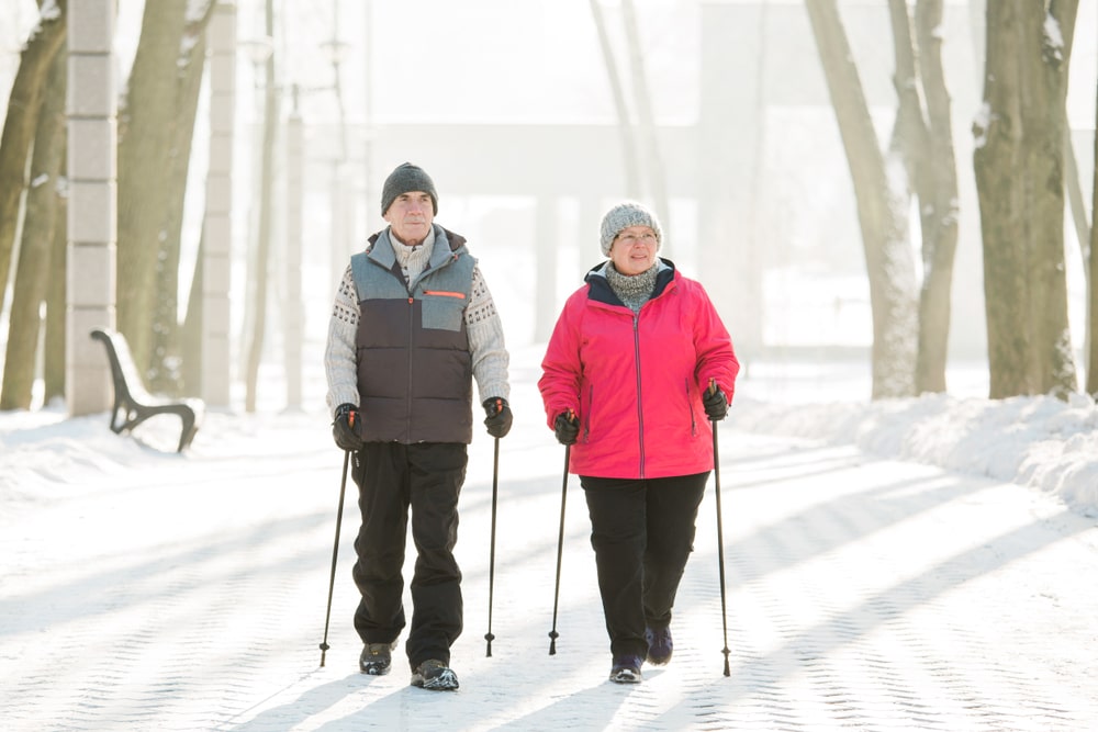A man and woman walking with ski poles on a snow-covered nature trail. 