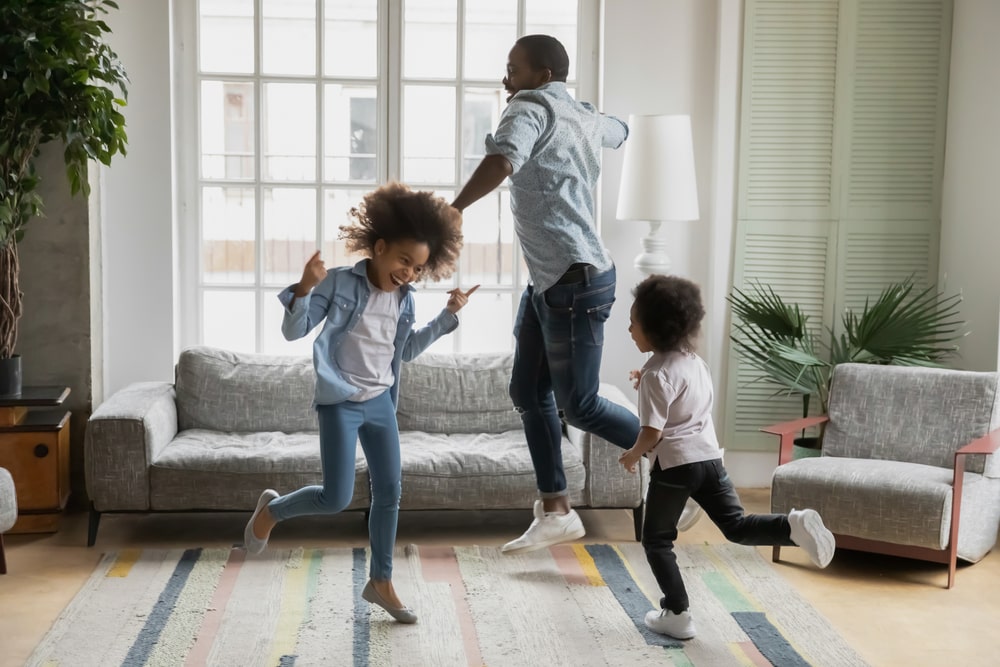 A father and his two daughters dancing in a living room. 