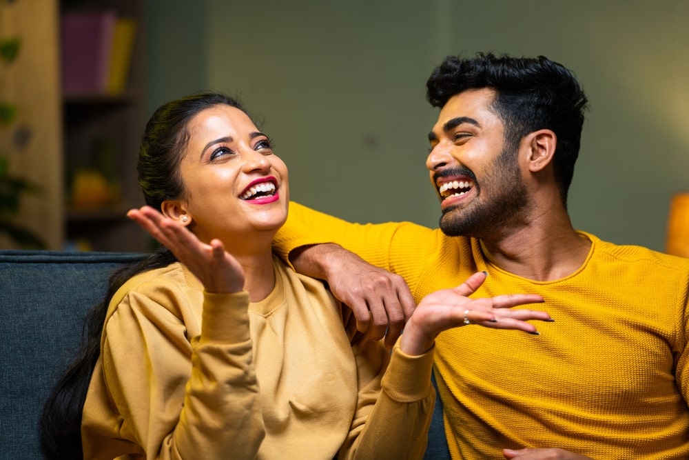 A woman and man laughing while sitting on a couch.