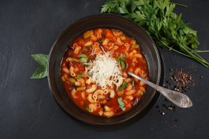 Un bol de soupe minestrone parsemé de fromage râpé et garni de persil.