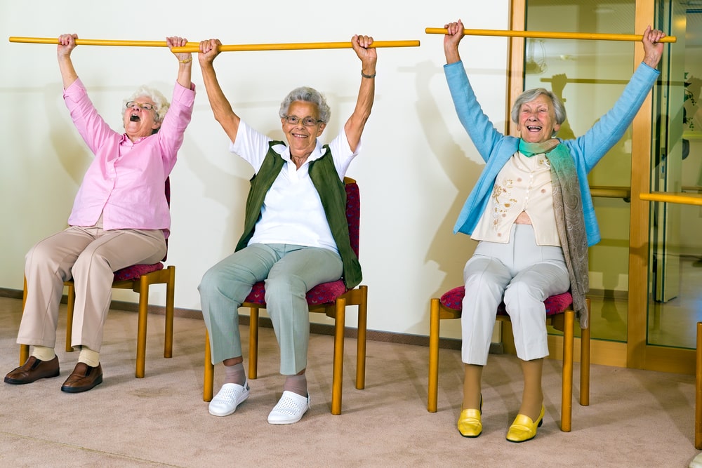 A group of older women sitting in chairs while lifting bars over their heads.