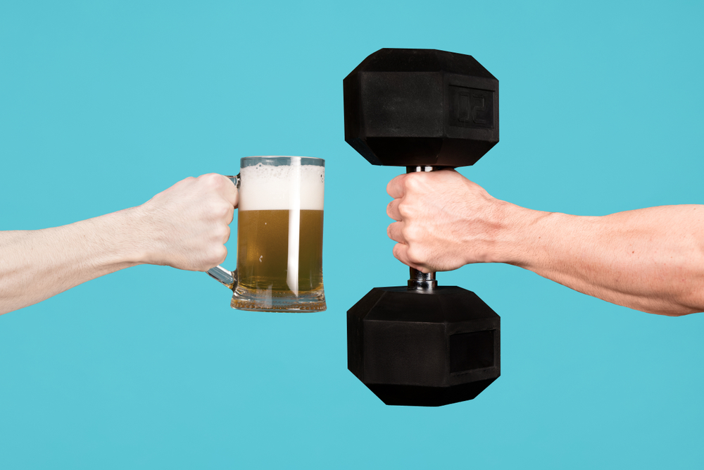 A hand holding a beer mug and another hand holding a dumbbell. 