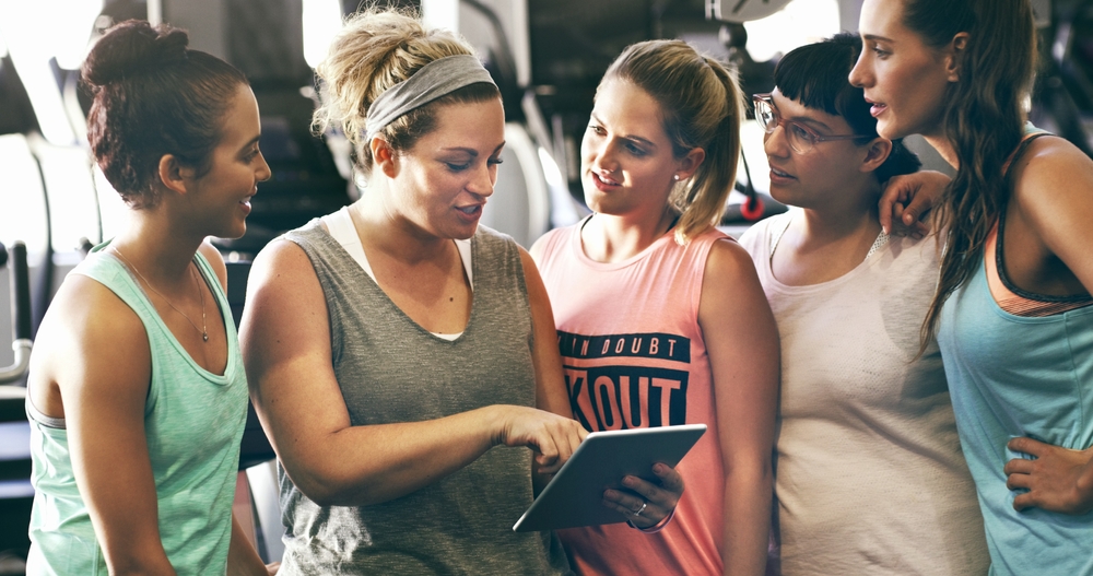 Un groupe de femmes dans un gymnase regardant une tablette. 