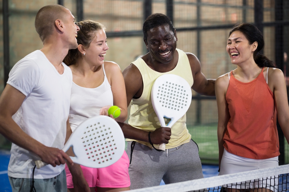  A group of smiling people holding pickleball rackets and balls. 