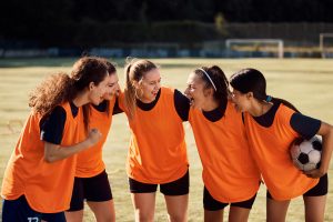 A team of female soccer players huddling on a soccer field.