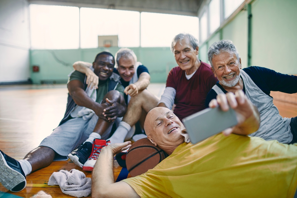 A group of older men taking a group selfie on a basketball court.