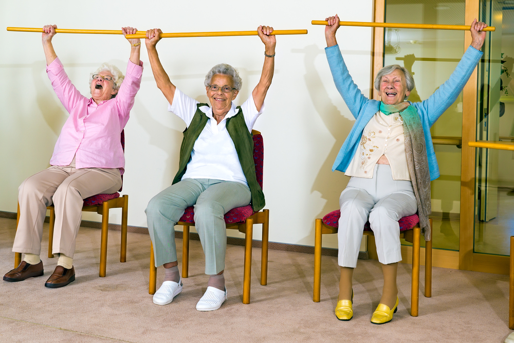 Un groupe de femmes âgées assises sur des chaises qui soulèvent des barres au-dessus de leur tête.