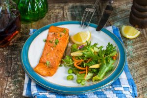 A maple-glazed salmon filet, lemon wedge and salad on a plate.