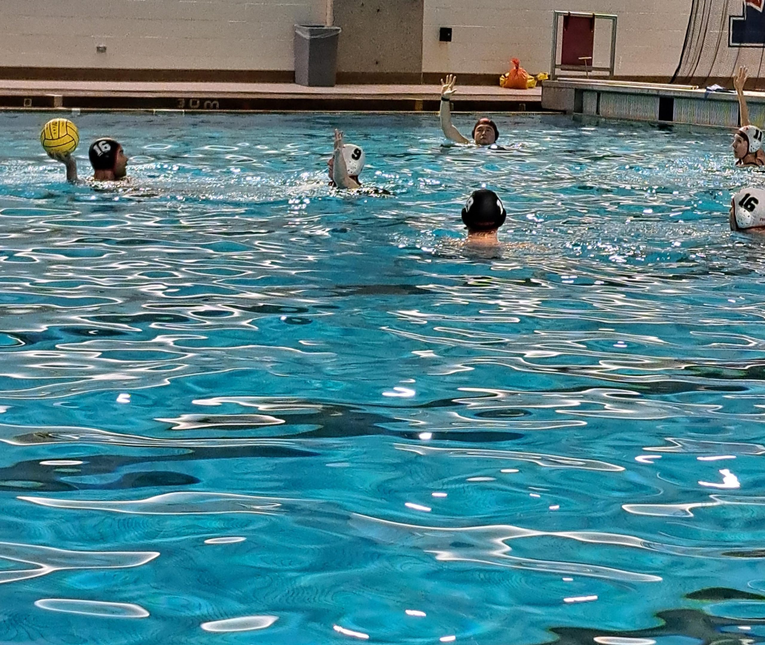 A group of people playing water polo in an indoor pool.