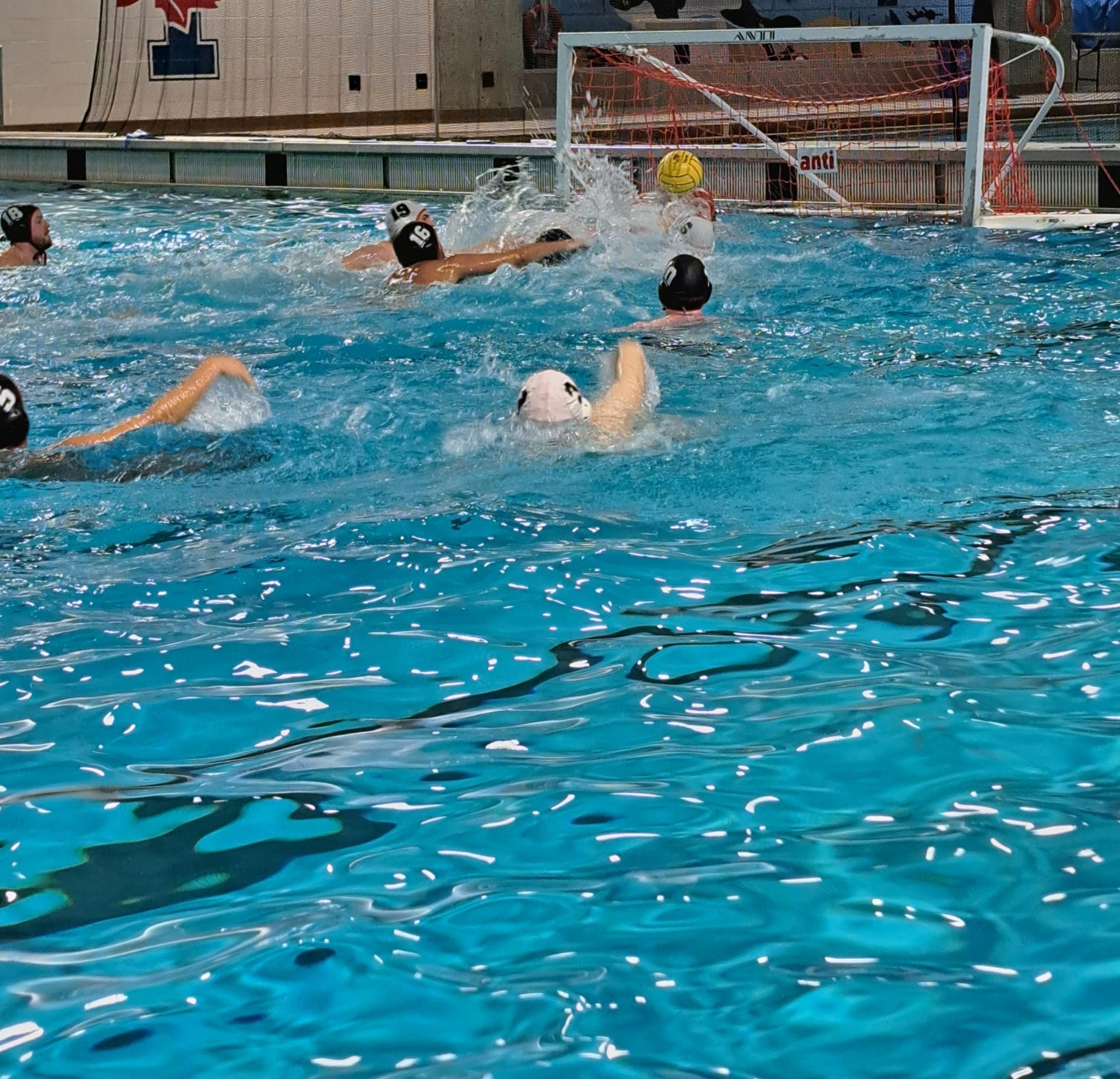 A group of people playing water polo in an indoor pool. 