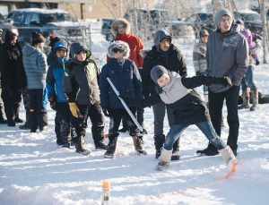 A group of kids playing the Dene game called snow snake in a snow-covered field.