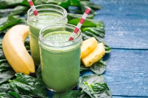 Two mason jars filled with green smoothies surrounded by a banana, pineapple pieces and spinach.