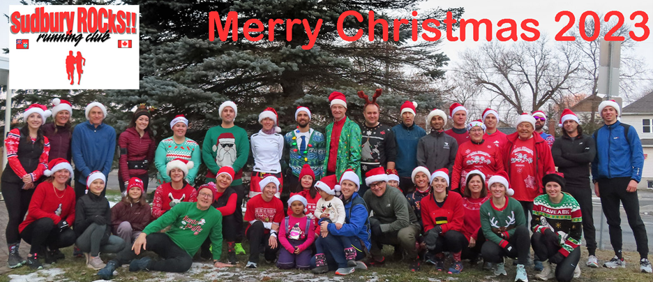 Un groupe de personnes portant des bonnets et des chandails de Noël posant pour une photo devant un conifère. 