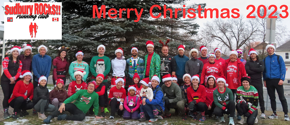 A group of people wearing Santa hats and Christmas sweaters posing for a photo in front of a conifer tree.