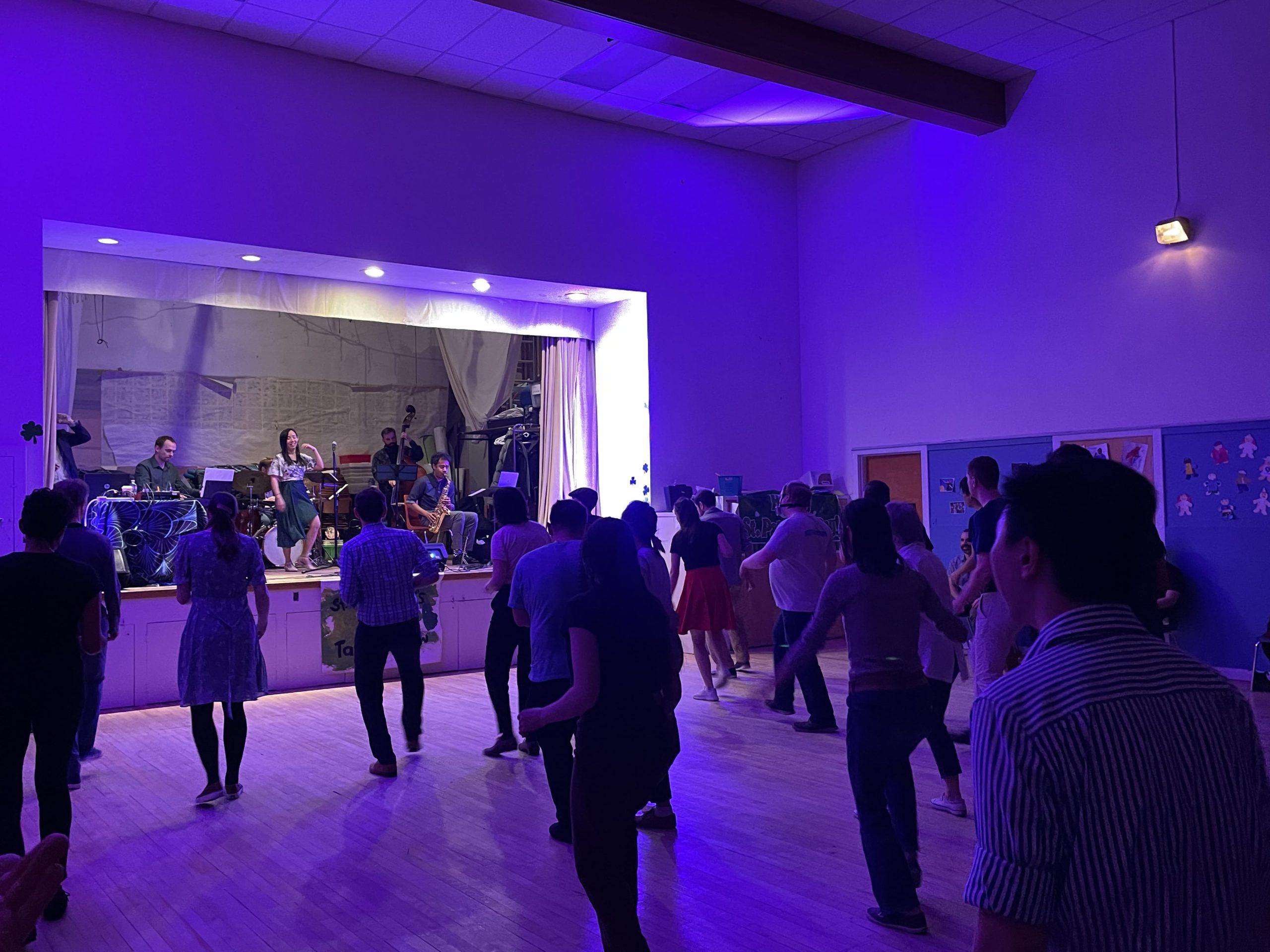 People dancing in a hall with a live band performing on stage.
