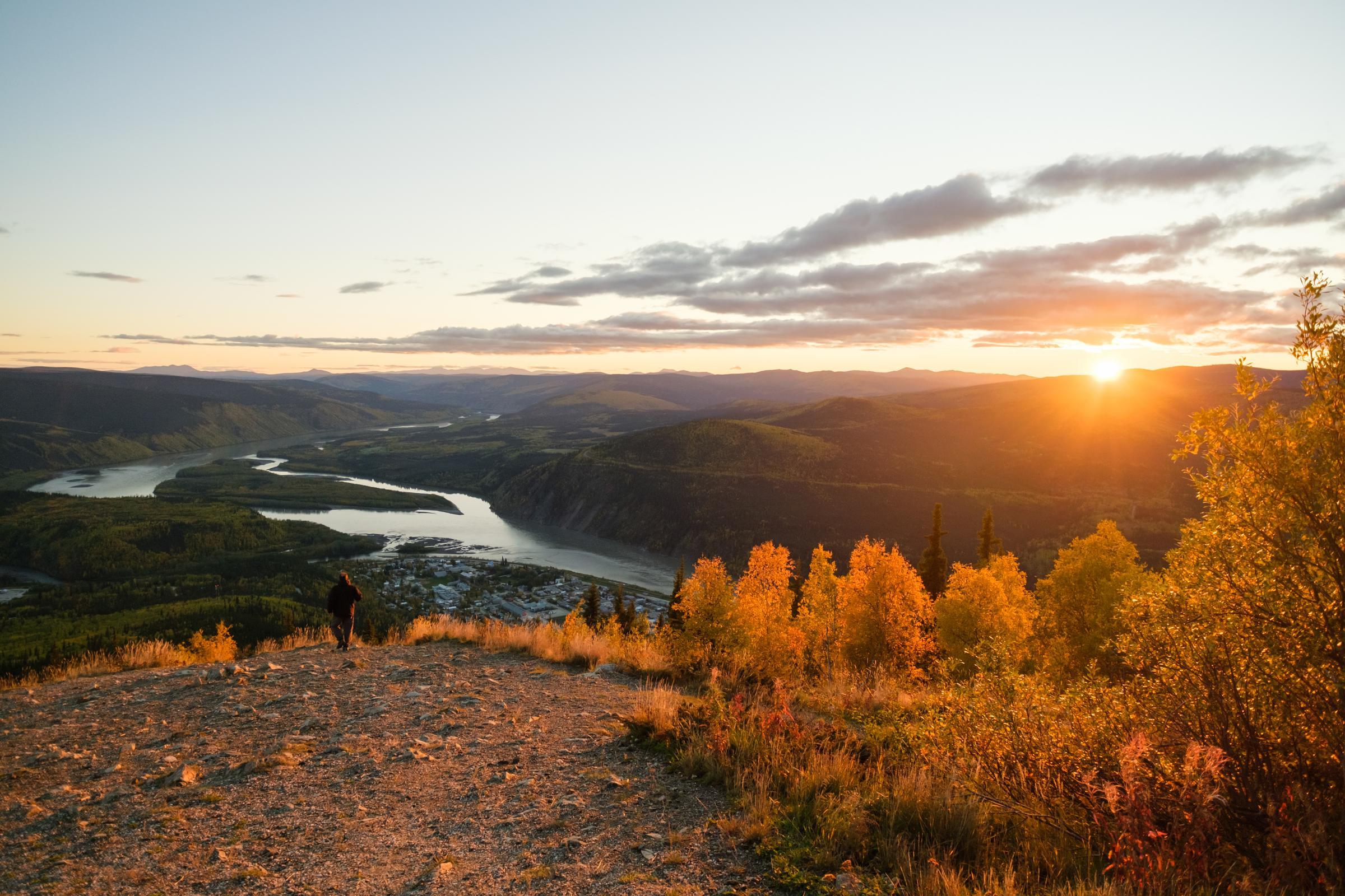A person hiking on a mountain overlooking a river at sunrise. A person hiking on a mountain overlooking a river at sunrise.