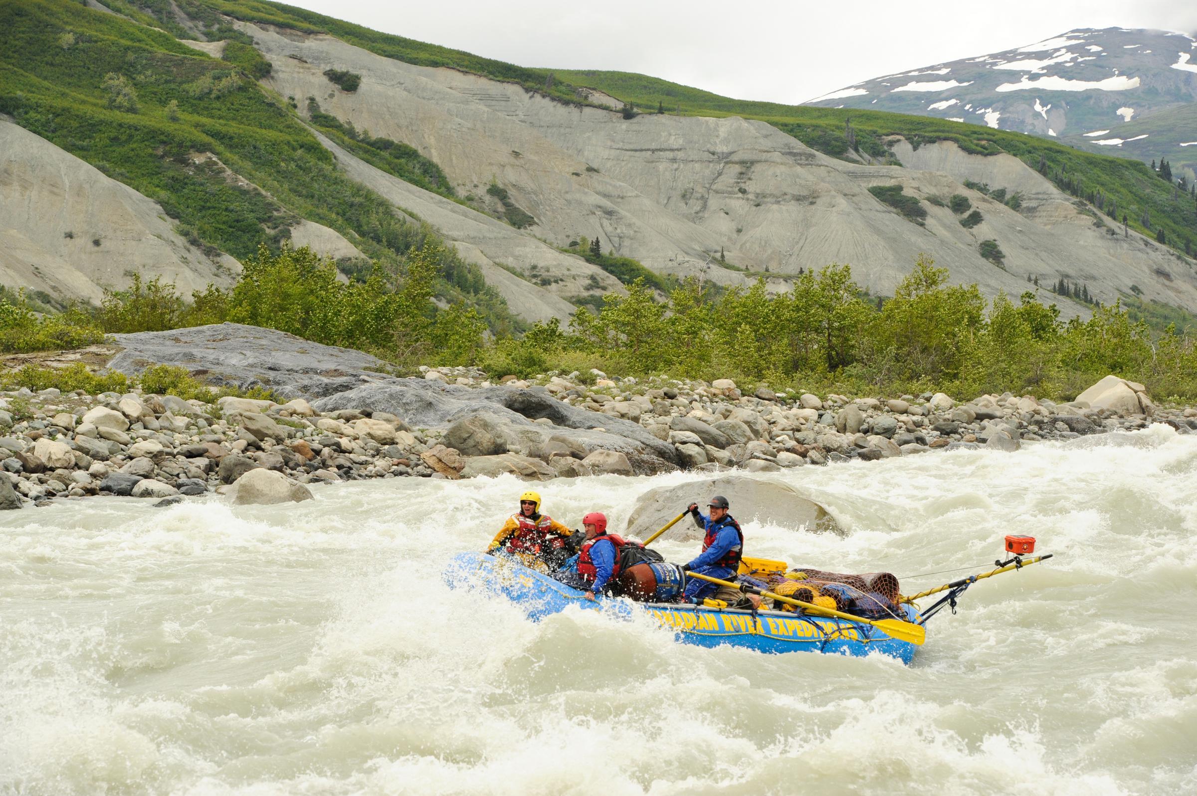 A group of people whitewater rafting beside a mountain. A group of people whitewater rafting beside a mountain.