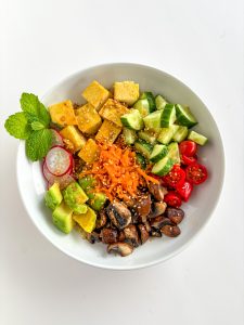 A bowl with tofu, cucumber, cherry tomatoes, mushrooms, carrot, avocado and radish.