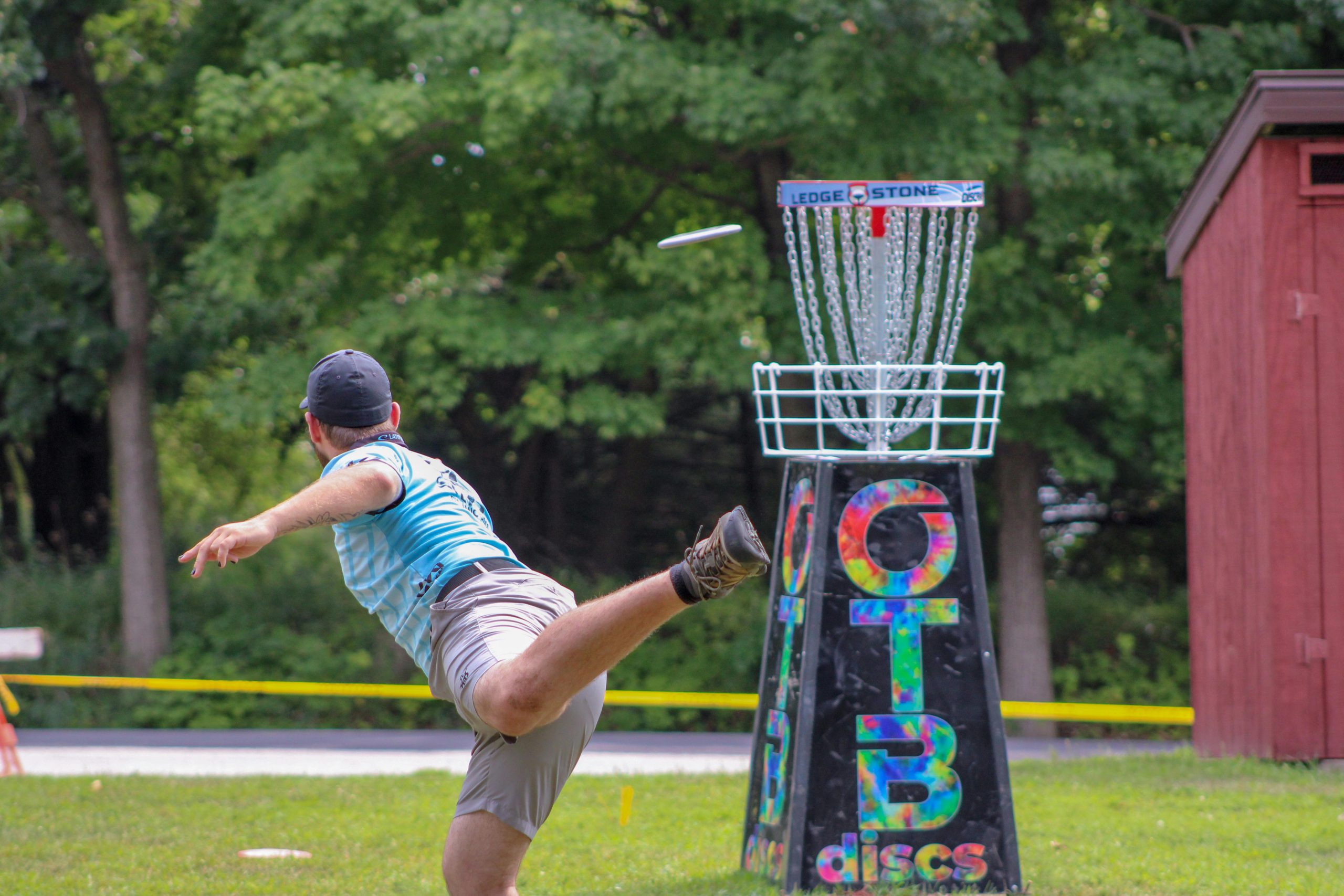 A man throwing a disc at a disc golf course basket target. A man throwing a disc at a disc golf course basket target.